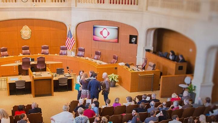 Government officials and community members gather together in council room for a hearing.